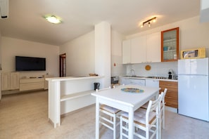 A modern kitchen with white cabinetry, a dining area with a white table and chairs, a flat-screen TV mounted on the wall, and a built-in microwave.