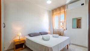 Een slaapkamer met een bed, nachtkastje, lamp en een raam met gordijnen.
