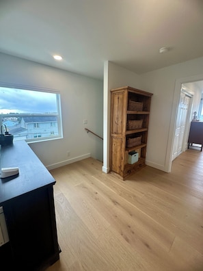 A room with a wooden bookshelf, a window with a view, and a dark wooden table. - Cloud Ninth - Ocean View Yachats (Yachats)