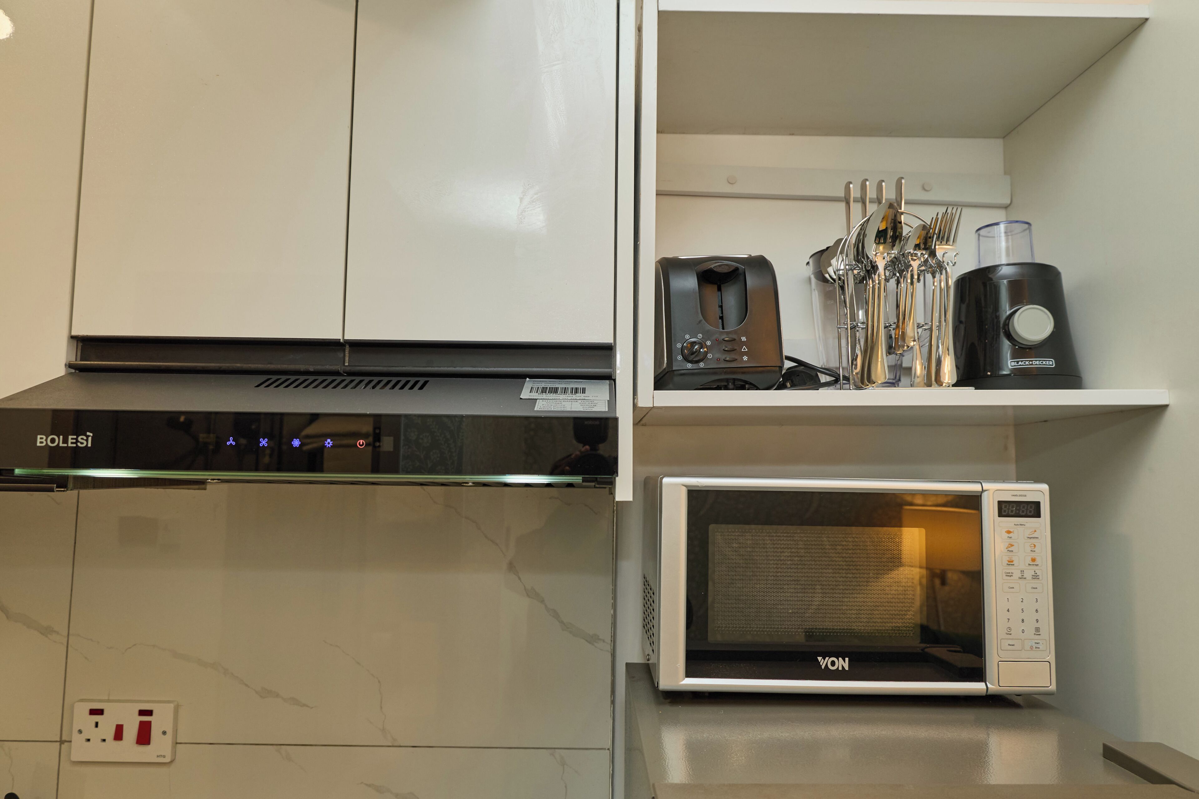 A kitchen with a microwave, a coffee maker, and utensils on a shelf.