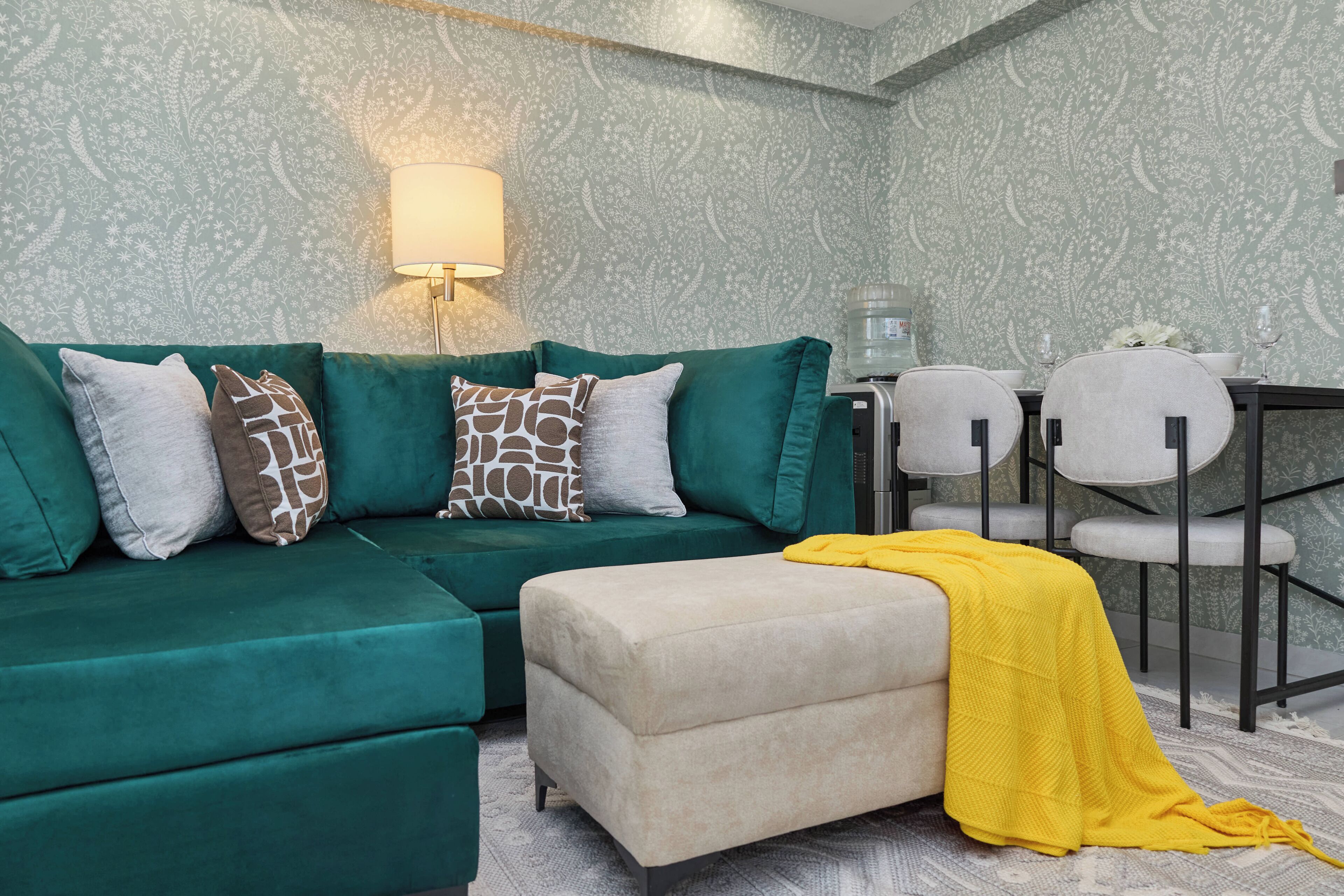 Un sofá verde con cojines estampados, un reposapiés color beige y una manta amarilla.
