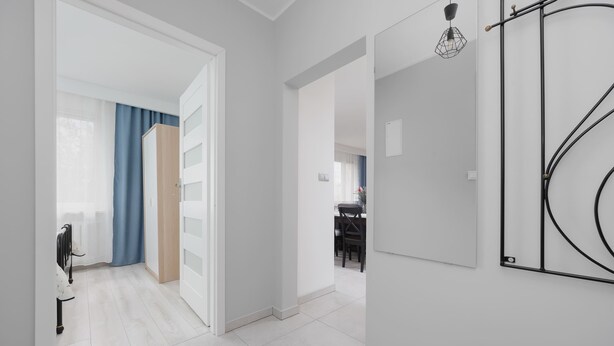 Un interior moderno con un pasillo que lleva a una habitación con cortina azul, un radiador y una zona de comedor al fondo.
