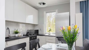 Una cocina moderna con armarios blancos, una mesa de comedor preparada para dos personas y un jarrón con flores.
