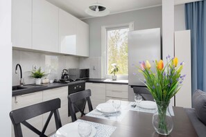 Una cocina moderna con armarios blancos, una mesa de comedor preparada para dos personas y un jarrón con flores.