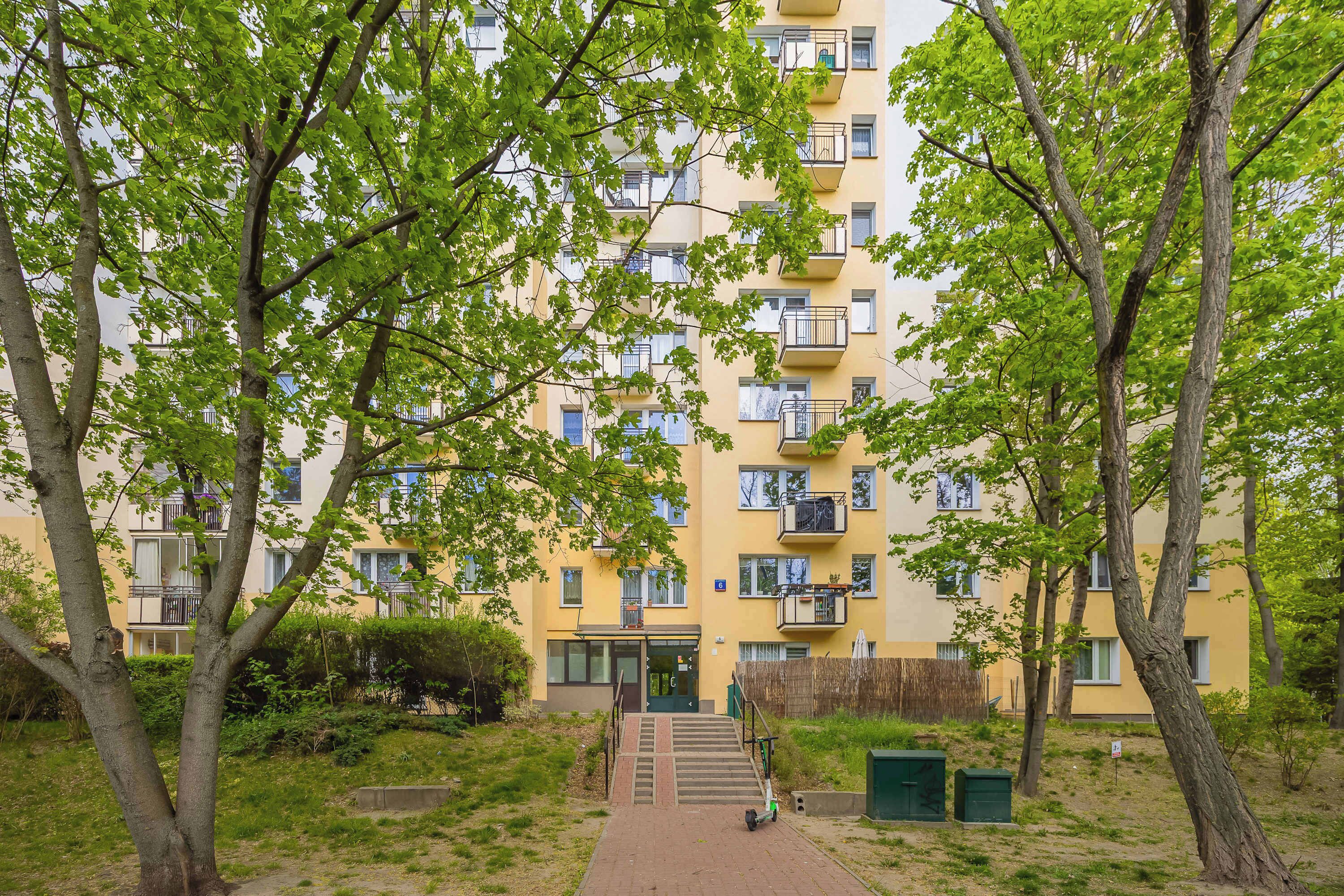 Een meerlaags woongebouw met balkons, een centrale ingang en een pad naar de ingang.
