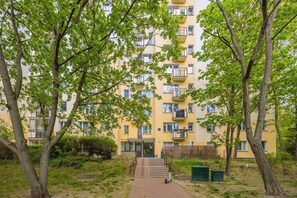 Un edificio residencial de varios pisos con balcones, una entrada central y un camino que lleva a ella.