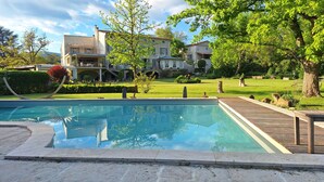 A swimming pool with a wooden deck, surrounded by a well-maintained lawn and mature trees. - Domaine de la Francoise (Dieulefit)