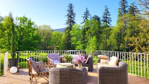 A deck with wicker furniture, a white railing, and a view of a green landscape with trees and hills. - Domaine de la Francoise (Dieulefit)