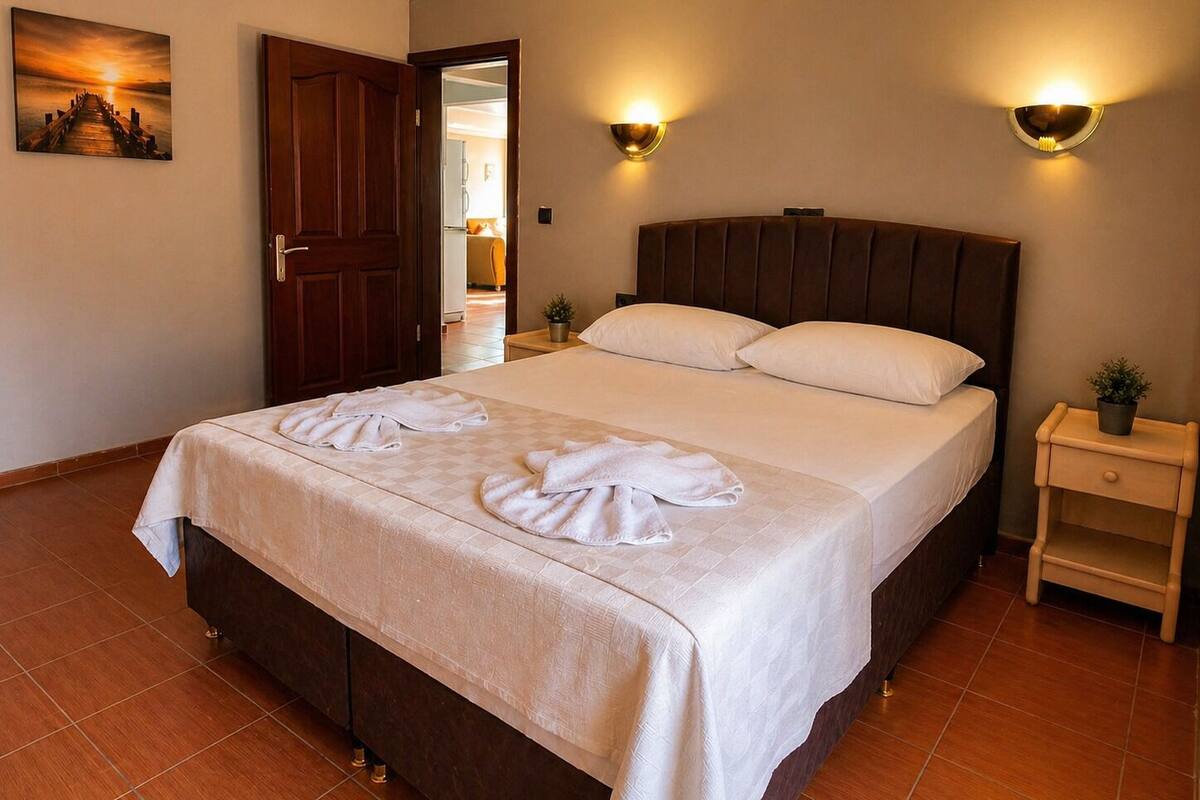 A hotel room with a bed, two wall sconces, a door, a painting, and a nightstand with a plant.