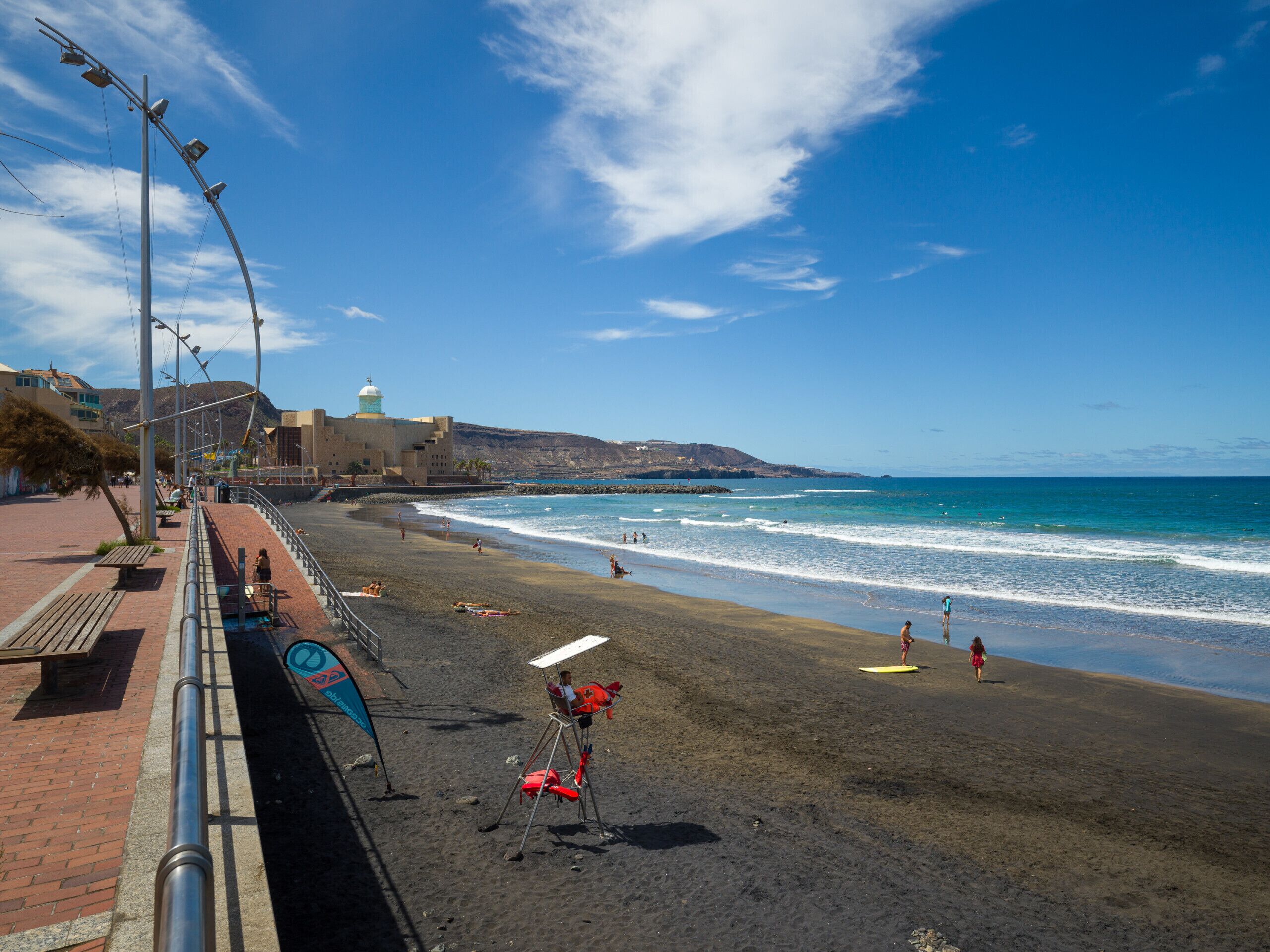 A beach with a paved walkway, benches, and a lifeguard chair.