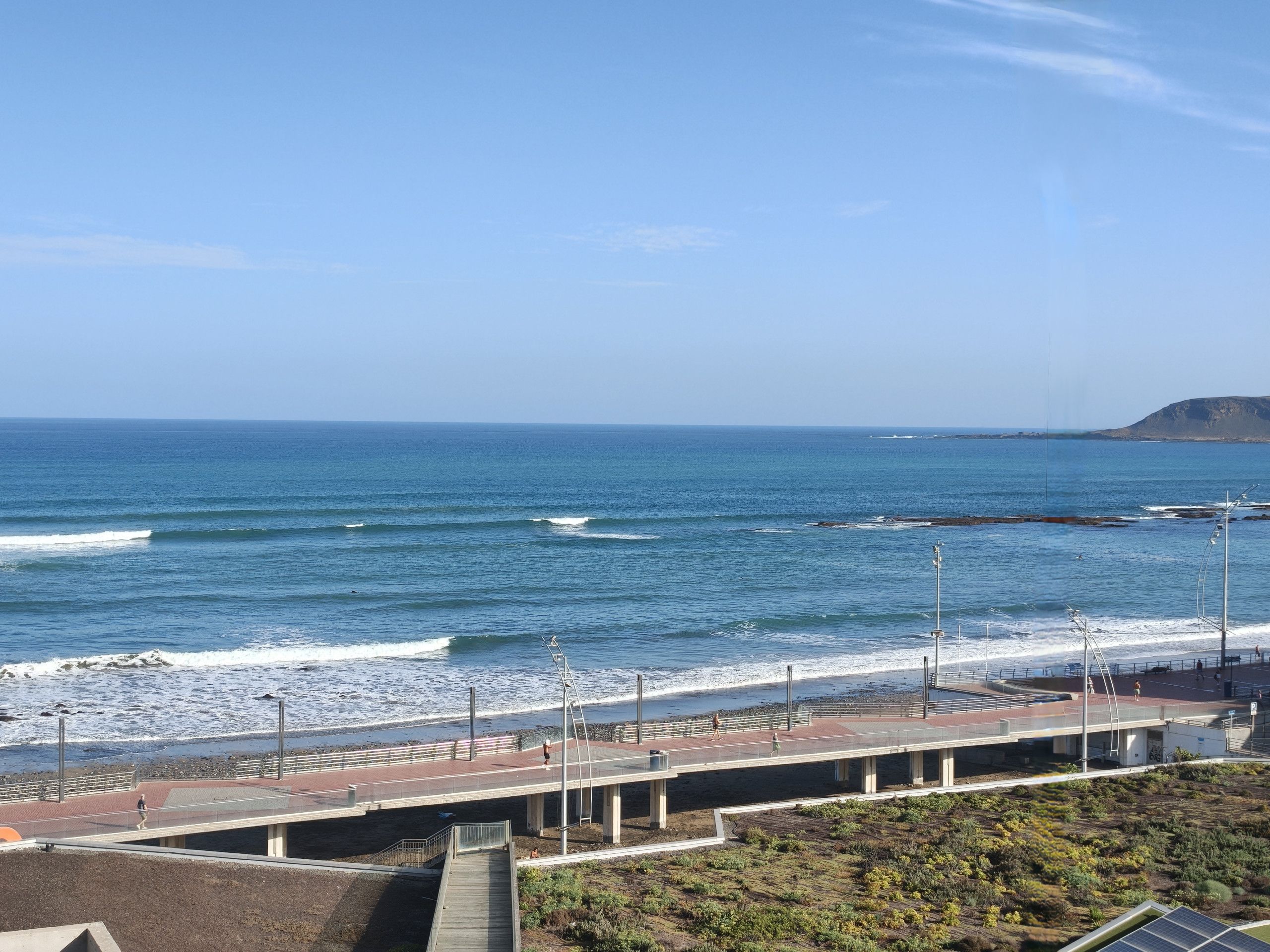 A coastal walkway with a view of the ocean and a distant hill.