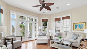 Amplia sala de estar con ventilador de techo, ventanas grandes y vistas al exterior.