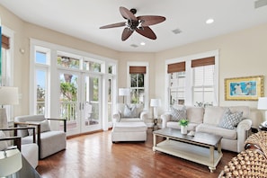 A spacious living room with a ceiling fan, large windows, and a view of the outdoors. - Just In Time |Lakefront in Destin Pointe | 3BR Coastal Escape w/ Beach Access (Destin)