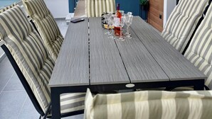 Uma área de refeições moderna ao ar livre com mesa de madeira, almofadas listradas, uma garrafa e copos.