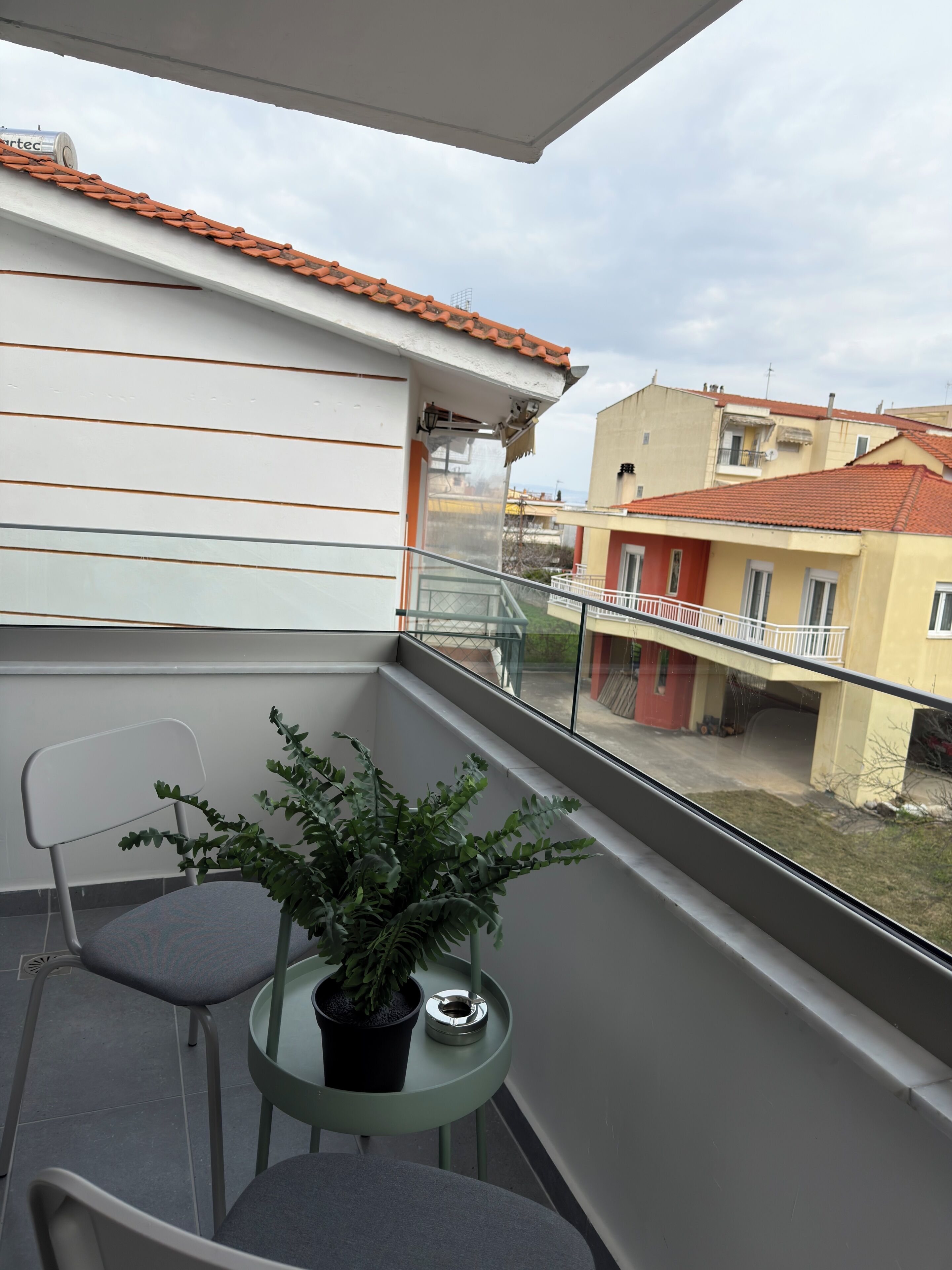 A balcony with a potted plant, two chairs, and a small table.