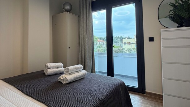 Quarto de hotel moderno com uma cama grande, um ventilador de teto, vista para o exterior e uma cômoda branca.