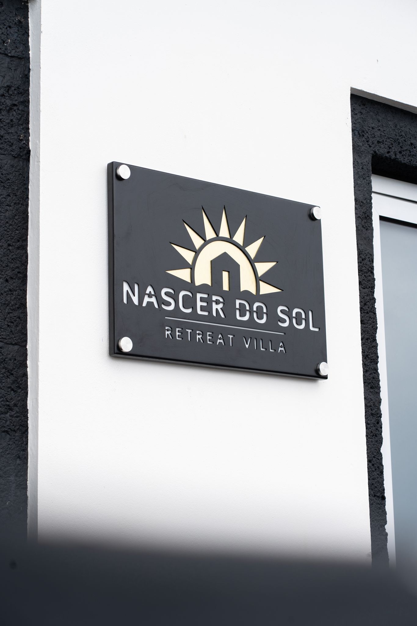 A sign for 'NASCER DO SOL RETREAT VILLA' with a sun and house logo.