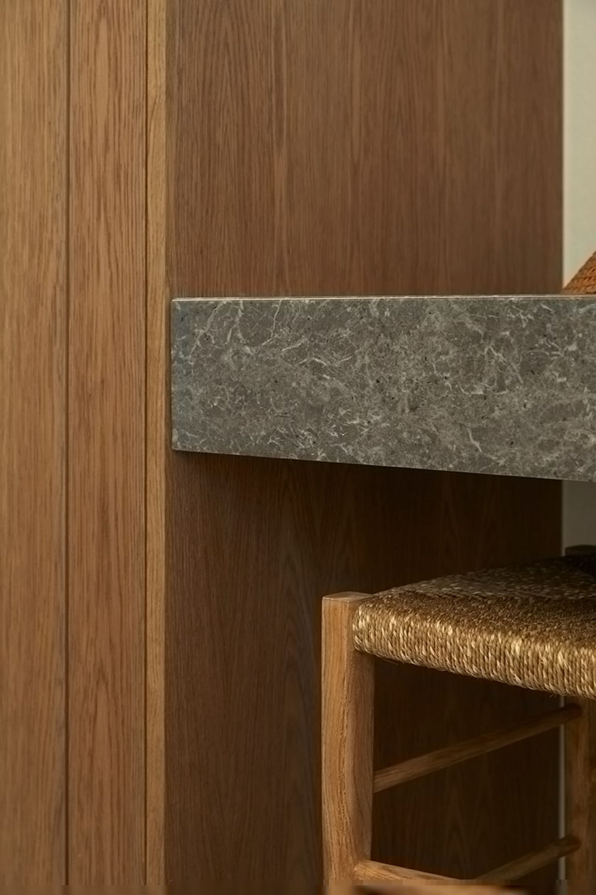 A wooden wall with a marble shelf and a woven chair.