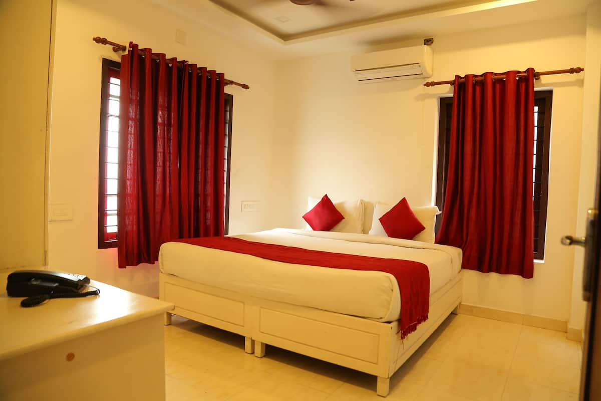 A bedroom with a bed, red curtains, a bedside table with a phone, and a window.