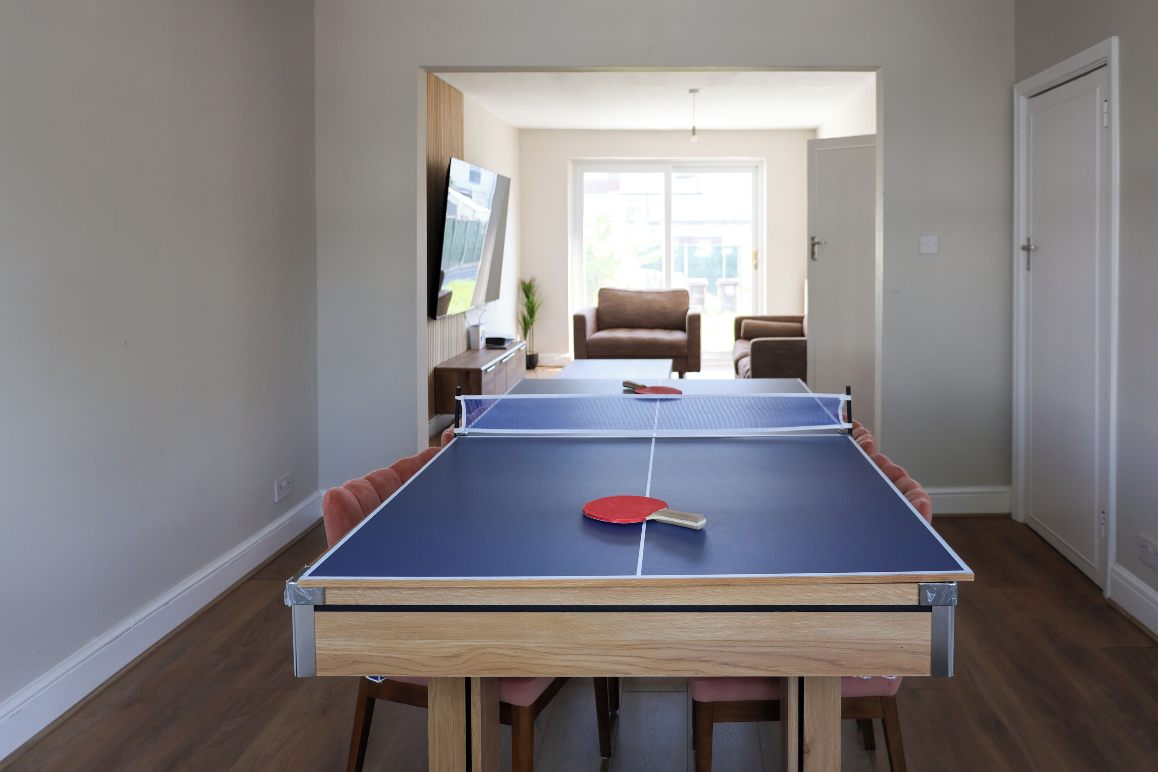 A ping pong table in a room with a TV, a couch, and a door.