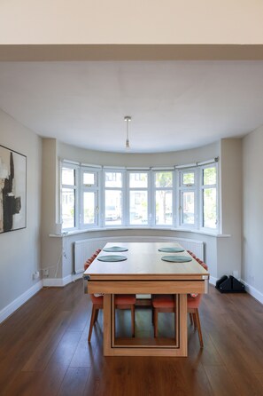 A dining area with a large table, chairs, and a bay window with multiple panes. - Modern Home with Pool Table Netflix and Free Parking (Harrow)