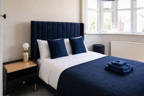 A bed with a dark headboard, white bedding, and a blue blanket. - Modern Home with Pool Table Netflix and Free Parking (Harrow)
