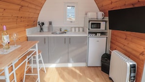 Una cocina compacta con lavabo, microondas y refrigerador, paredes de madera y un reloj en la pared.