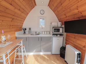 Una cocina compacta con lavabo, microondas y refrigerador, paredes de madera y un reloj en la pared.