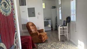 Una sala de estar con un sillón marrón, un sofá rojo, un tapete estampado, una mesa blanca y un ordenador portátil sobre una silla.