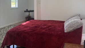 Un dormitorio con una cama, ventilador de techo, ventana y una mesita.