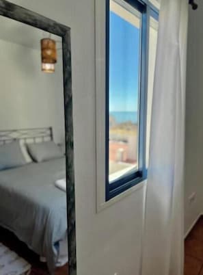 Ein Schlafzimmer mit Bett, einem Fenster mit Blick und einem Spiegel an der Wand.