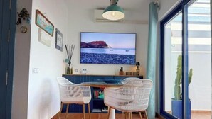 Un comedor con televisión, sillas de mimbre y vistas al mar a través de un ventanal grande.