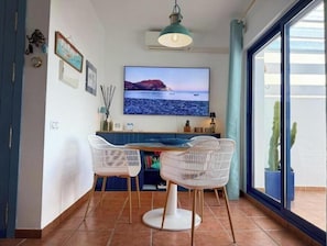 Ein Essbereich mit Fernseher, Korbstühlen und Meerblick durch ein großes Fenster.
