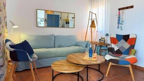 Un salón con sofá, dos sillones, una mesa redonda, una lámpara colgante, un espejo y una mesita con lámpara.