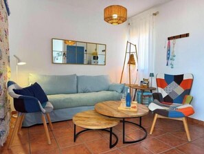 Ein Wohnzimmer mit einer Couch, zwei Sesseln, einem runden Couchtisch, einer Hängeleuchte, einem Spiegel und einem kleinen Tisch mit Lampe.