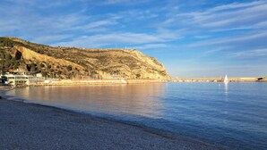 A coastal beach with a pebbly shore, a hill with sparse vegetation, and a clear sky. - Elegant Villa in Moraira for 6 · Private Pool Close to Town – ALMARE (Teulada)