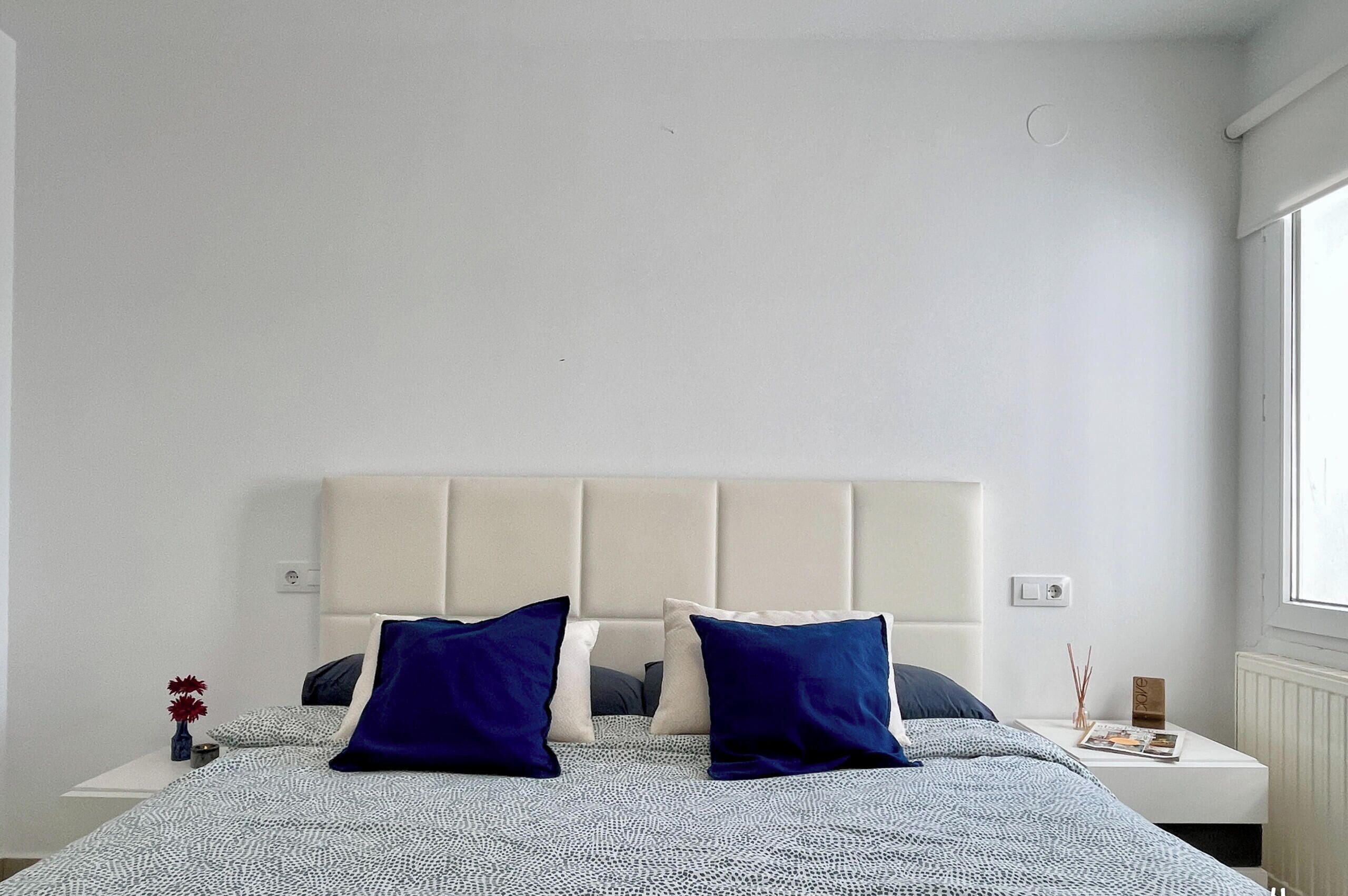 A bedroom with a bed, two pillows, a nightstand, a vase with flowers, and a window.