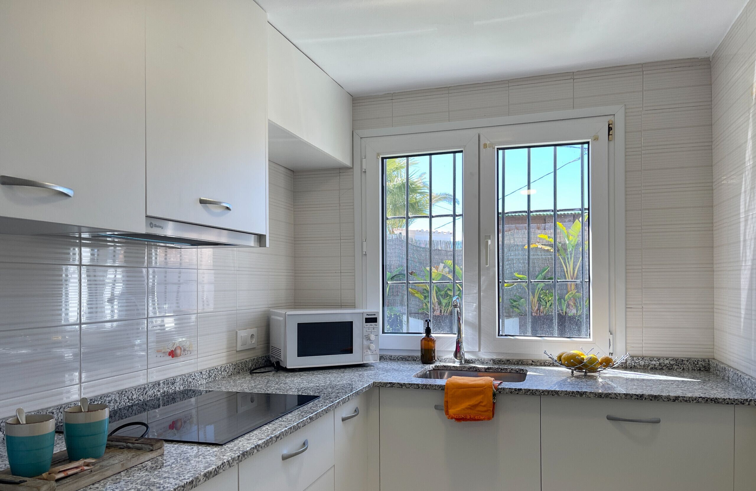 A modern kitchen with white cabinets, a microwave, a sink, and a window with a view of greenery.