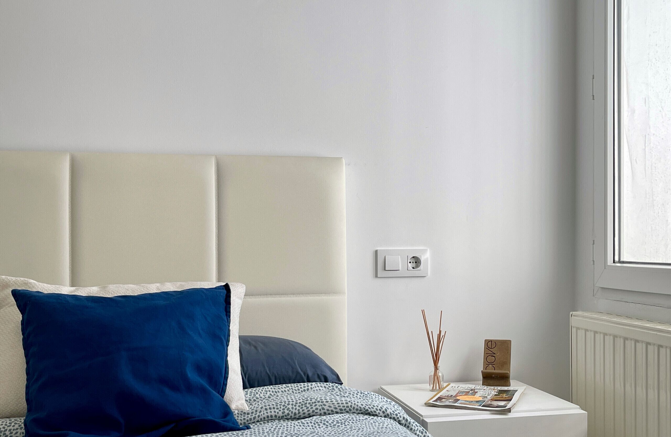 Une chambre à coucher avec un lit, une table de chevet, une fenêtre et un interrupteur mural.