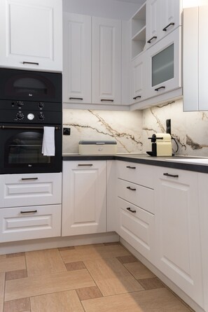 A kitchen with white cabinets, a black oven, a marble backsplash, and a coffee machine. - Sweet View (Paros)