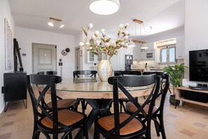 A modern dining area with a glass table, black chairs, and a vase with flowers. - Sweet View (Paros)