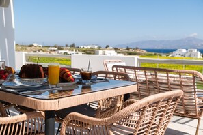 A table with wicker chairs, a glass table, and a view of the sea and mountains. - Sweet View (Paros)