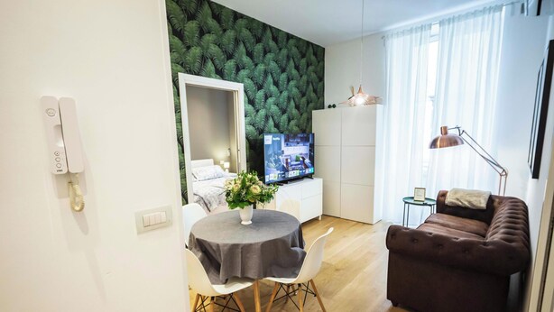 Moderni olohuone, jossa on ruokailutila, sohva, televisio ja vihreäkuvioinen seinä.