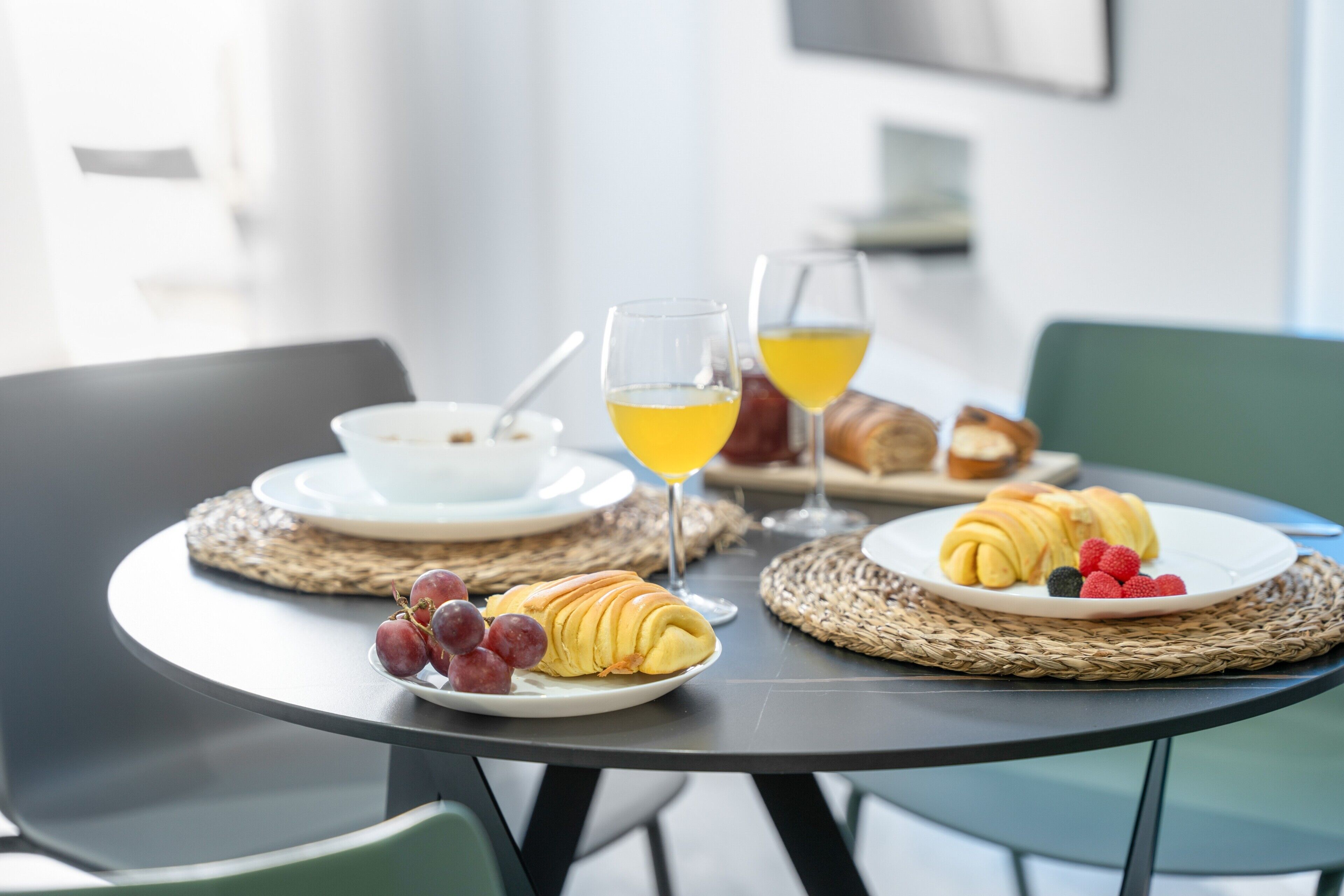 Une table à manger avec des assiettes remplies de nourriture, des verres de jus de fruits et un croissant.