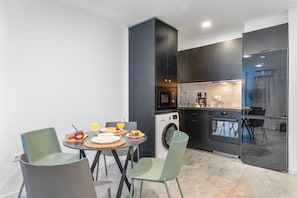 Een kleine keuken met een wasmachine, een eethoek met stoelen en een ontbijttafel gedekt.