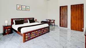 A bedroom with a large bed, a nightstand, a chair, a table, and two wooden doors. - NON AC Saver Hotel O Mehta College (Amer)