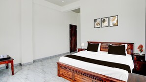 A bedroom with a large bed, a wooden nightstand, a bedside table, a door, and a wall with three framed pictures. - NON AC Saver Hotel O Mehta College (Amer)