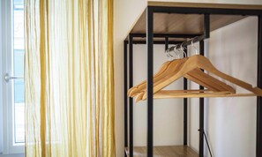 Een kamer met een metalen kledingkast, een houten kleerhanger en een raam met jaloezieën.