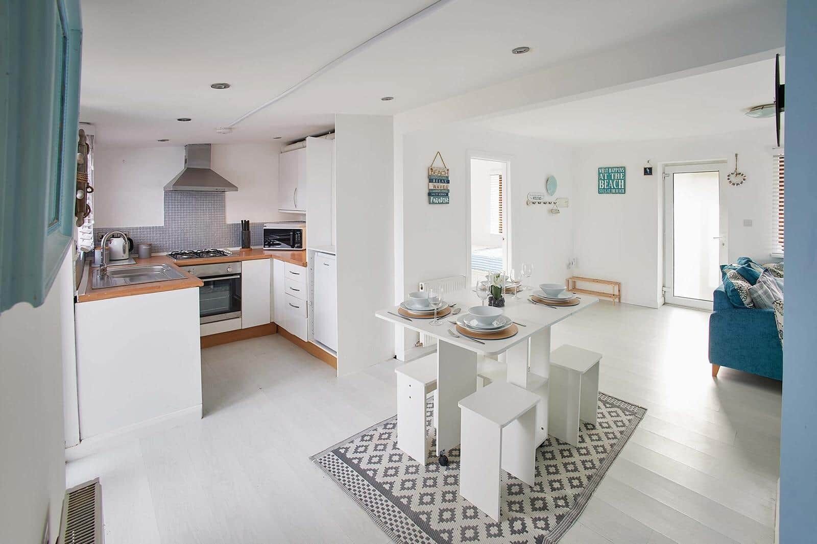 A modern kitchen with white cabinetry, a dining area with a white table, and a blue sofa in the living room.