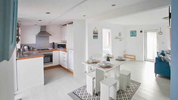Una cocina moderna con muebles blancos, un comedor con mesa blanca y un sofá azul en la sala.